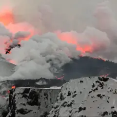 Glödande lava strömmar nerför en snötäckt sluttning, omgiven av tjock rök. Ett dramatiskt exempel på vulkaner i Europa.