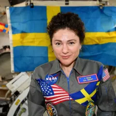 Astronaut med svensk flagga bakom sig. Hon bär en dräkt med både amerikanska och svenska symboler, vilket visar att svenskar i rymden är en del av internationellt samarbete.