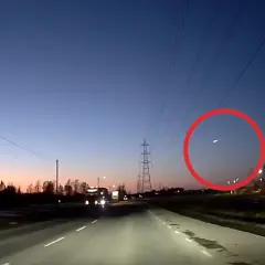 En ljusstark meteor syns på den mörka himlen över en väg i Sverige.