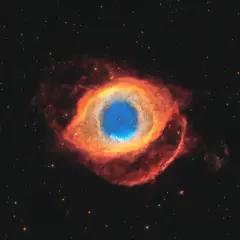 Helixnebulosan, ett kosmiskt öga av gas och stoft, lyser i rött och blått mot en stjärnbeströdd rymd.