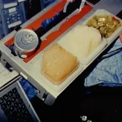 En astronaut äter rymdmat från en bricka. Maten ser ut som en burk, en gelé och en grönsaksrätt.