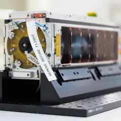 En satellit från Saab Aerospace, redo för rymden. En vit etikett med texten "REMOVE BEFORE FLIGHT" är fäst vid enheten.