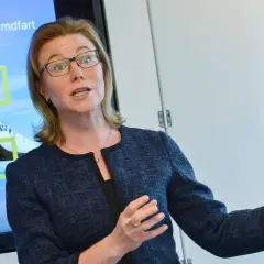 Karin Nilsdotter, med glasögon, gestikulerar vid en skärm som visar "Forskning" och "Satelliter" i samband med rymdfart.