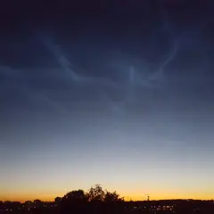 Mörka moln med ljusa strimmor, nattlysande moln, över en stad i skymningen.