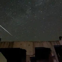 En ljus meteor drar en strimma över en stjärnklar natthimmel, ovanför ruinerna av en byggnad.