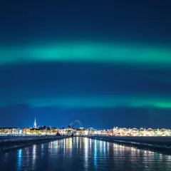 Luleå norrsken lyser upp himlen över en stad vid en isig kustlinje.