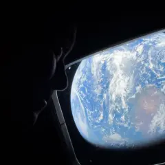 Silhuett av en person som tittar ut genom ett fönster på jorden från rymden. ISS Sverige.