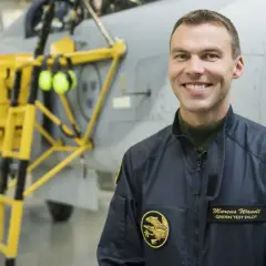 Marcus Wandt, Gripen testpilot, ler glatt framför ett stridsflygplan.