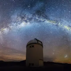 En kupolformad observatoriebyggnad står under en magnifik vintergatan från jorden. Stjärnorna lyser starkt mot den mörka himlen.