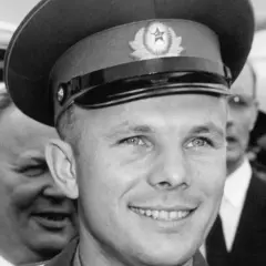 Juri Gagarin, den första människan i rymden, ler mot kameran. Han bär en rymdkeps med en sovjetisk symbol.