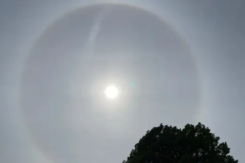 En vacker solring runt solen, ett optiskt fenomen som skapar en cirkel av ljus. En grönaktig prick syns också nära solen.