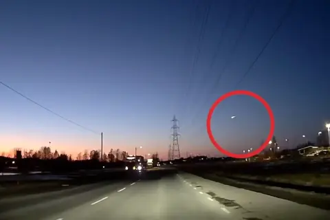 En ljusstark meteor syns på den mörka himlen över en väg i Sverige.
