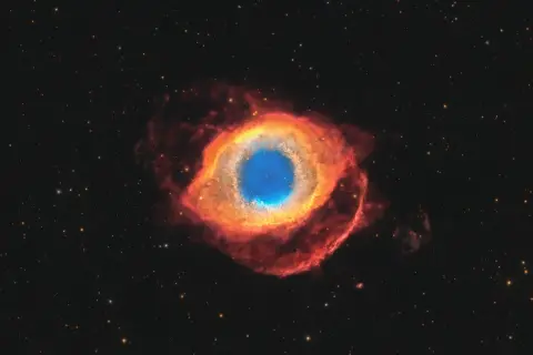 Helixnebulosan, ett kosmiskt öga av gas och stoft, lyser i rött och blått mot en stjärnbeströdd rymd.