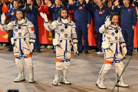 Astronaut Kina vinkar glatt till publiken i sin rymddräkt.