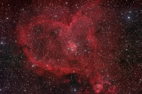 Ett kosmiskt hjärta av rött gasmoln och stjärnor, en hjärtnebulosa som lyser i rymden.