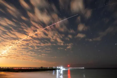 Långa ljusstrimmor på natthimlen, som visar satelliter runt jorden, med moln som drar förbi och stjärnor som glimmar.