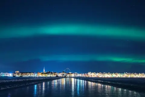 Luleå norrsken lyser upp himlen över en stad vid en isig kustlinje.