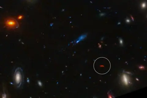 En avlägsen galax, likt en glödande orion nebulosan, lyser i mörkret bland andra kosmiska objekt.