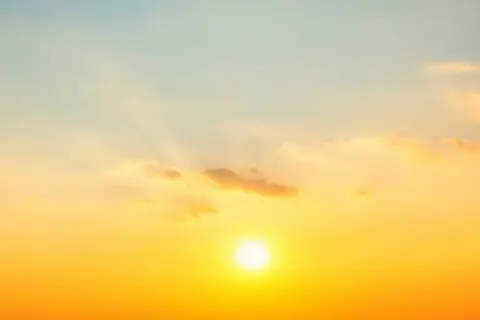 Solens strålar lyser upp himlen i en varm, gyllene ton. Molnen är mjuka och rosa, som om de fångar solnedgångens magi. En perfekt bild av sommarsolståndet.