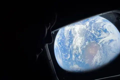 Silhuett av en person som tittar ut genom ett fönster på jorden från rymden. ISS Sverige.