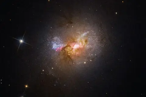 En galax med lysande gasmoln och stjärnor, liknande de magellanska molnen, lyser upp den mörka rymden.