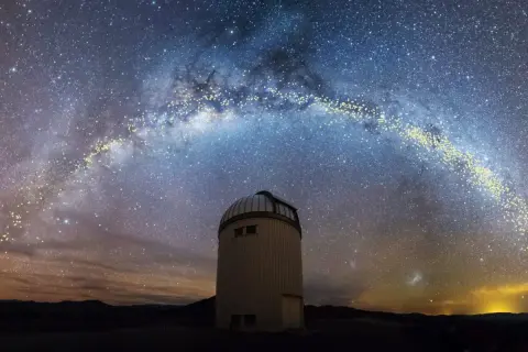 En kupolformad observatoriebyggnad står under en magnifik vintergatan från jorden. Stjärnorna lyser starkt mot den mörka himlen.