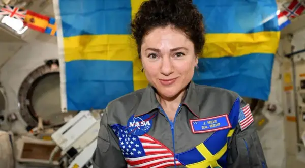 Astronaut med svensk flagga bakom sig. Hon bär en dräkt med både amerikanska och svenska symboler, vilket visar att svenskar i rymden är en del av internationellt samarbete.