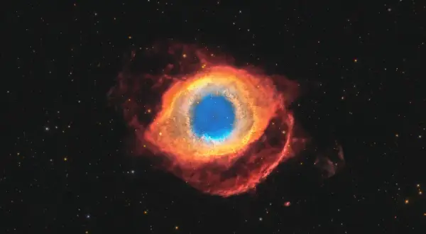 Helixnebulosan, ett kosmiskt öga av gas och stoft, lyser i rött och blått mot en stjärnbeströdd rymd.