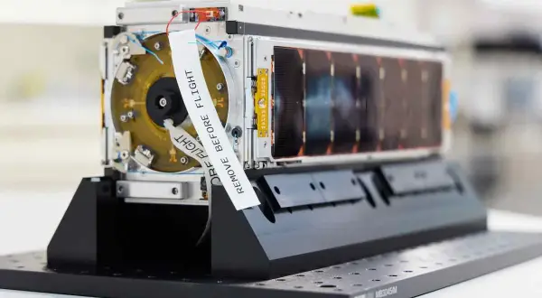 En satellit från Saab Aerospace, redo för rymden. En vit etikett med texten "REMOVE BEFORE FLIGHT" är fäst vid enheten.