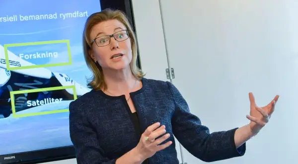 Karin Nilsdotter, med glasögon, gestikulerar vid en skärm som visar "Forskning" och "Satelliter" i samband med rymdfart.
