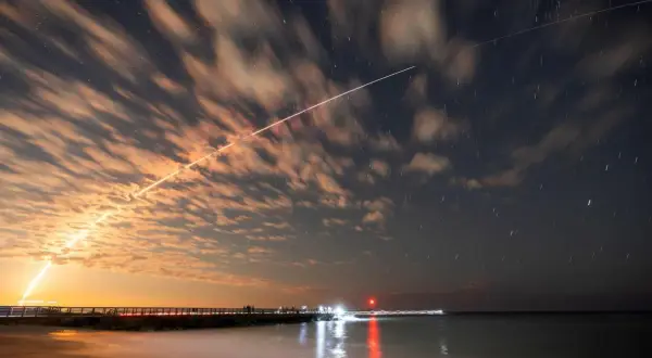 Långa ljusstrimmor på natthimlen, som visar satelliter runt jorden, med moln som drar förbi och stjärnor som glimmar.