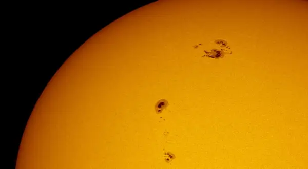 Solfläckar syns på solens yta, mörka områden som vittnar om solens ålder och aktivitet.