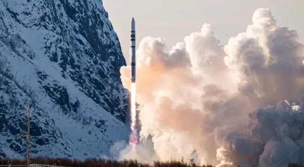 ISAR Aerospace raket skjuter upp från en snötäckt mark, med en snöig bergssida och moln i bakgrunden.