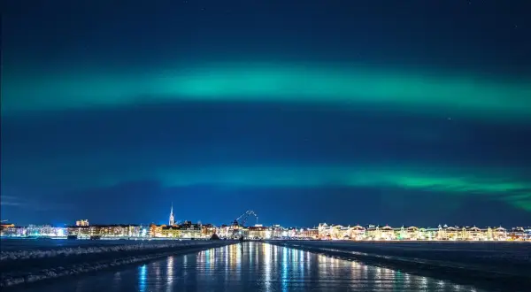 Luleå norrsken lyser upp himlen över en stad vid en isig kustlinje.