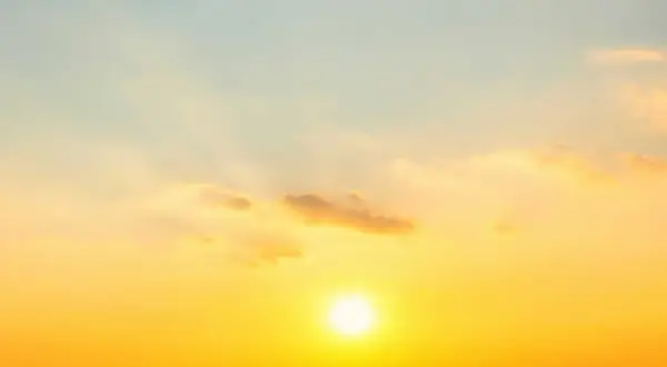 Solens strålar lyser upp himlen i en varm, gyllene ton. Molnen är mjuka och rosa, som om de fångar solnedgångens magi. En perfekt bild av sommarsolståndet.