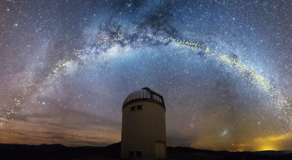 En kupolformad observatoriebyggnad står under en magnifik vintergatan från jorden. Stjärnorna lyser starkt mot den mörka himlen.