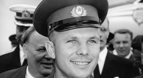 Juri Gagarin, den första människan i rymden, ler mot kameran. Han bär en rymdkeps med en sovjetisk symbol.