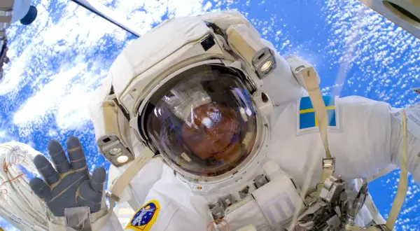 Astronaut med svensk flagga på dräkten, vinkar från rymden. Här arbetade Fuglesang på.