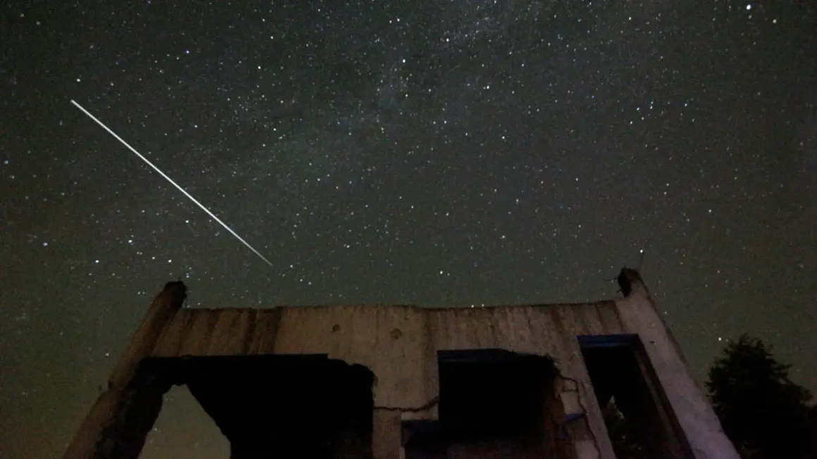 En ljus meteor drar en strimma över en stjärnklar natthimmel, ovanför ruinerna av en byggnad.