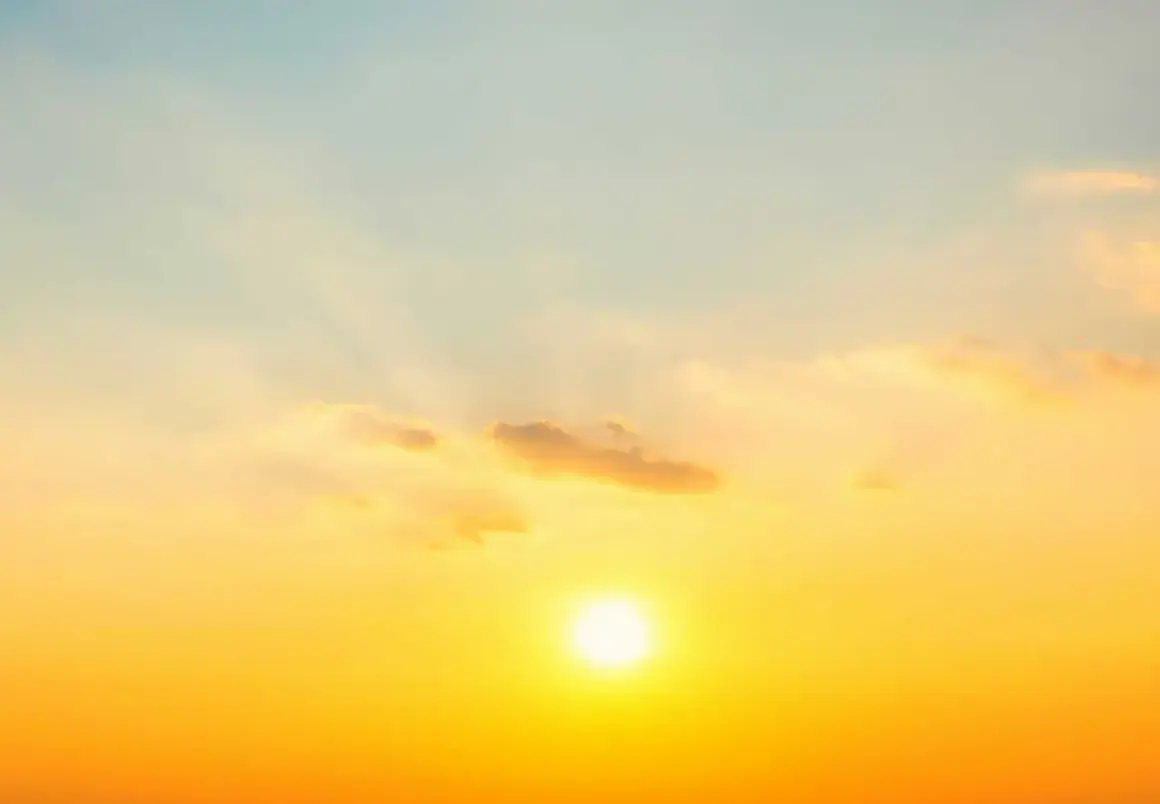 Solens strålar lyser upp himlen i en varm, gyllene ton. Molnen är mjuka och rosa, som om de fångar solnedgångens magi. En perfekt bild av sommarsolståndet.