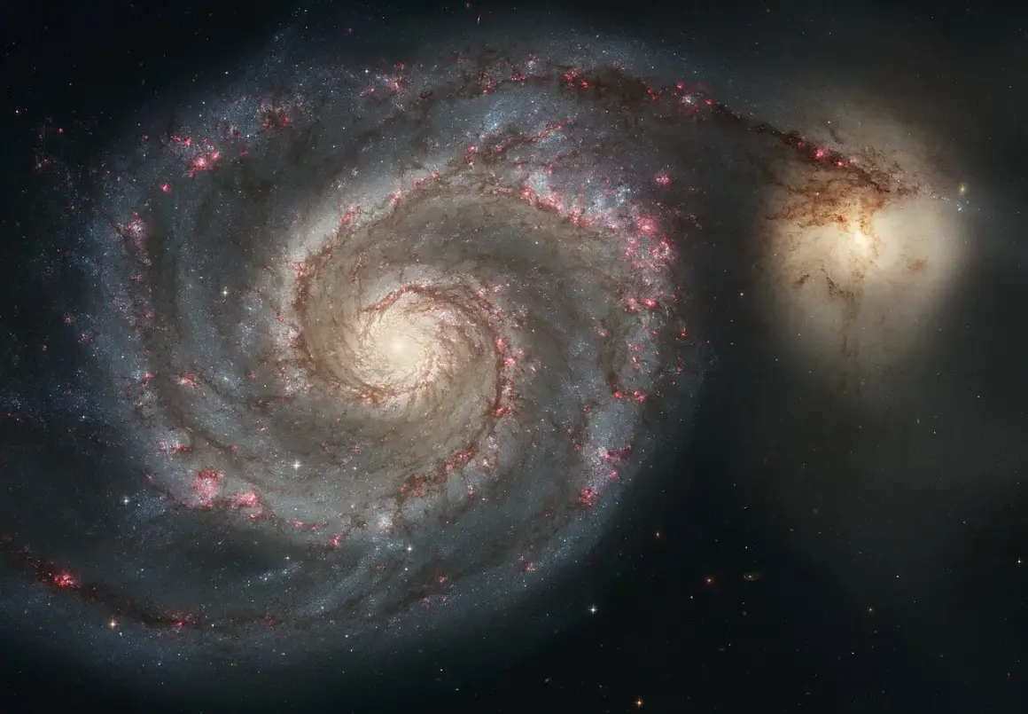 Två galaxer i en kosmisk dans. Den större, en spiralgalax med lysande armar, interagerar med en mindre, oregelbunden galax. Dessa former på galaxer visar universums dynamik.
