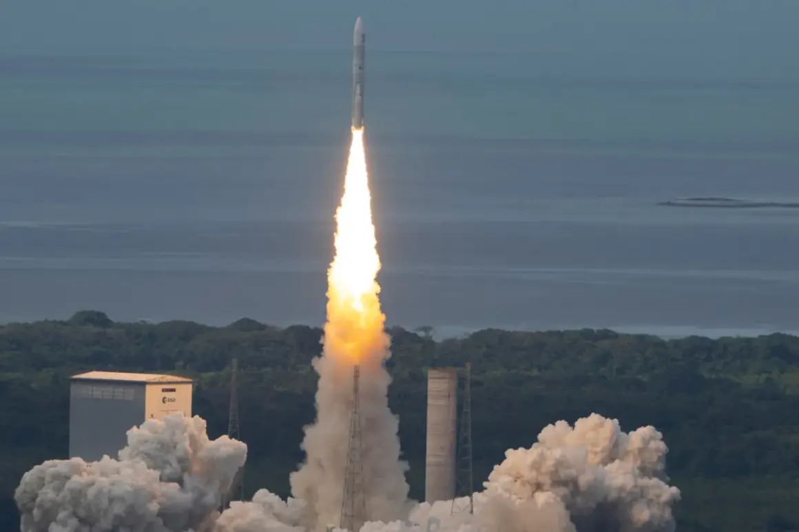 Ariane 5 skjuter upp från marken med en enorm eldsvåda och rök. Raketen stiger mot en blå himmel över ett grönt landskap och ett lugnt hav.