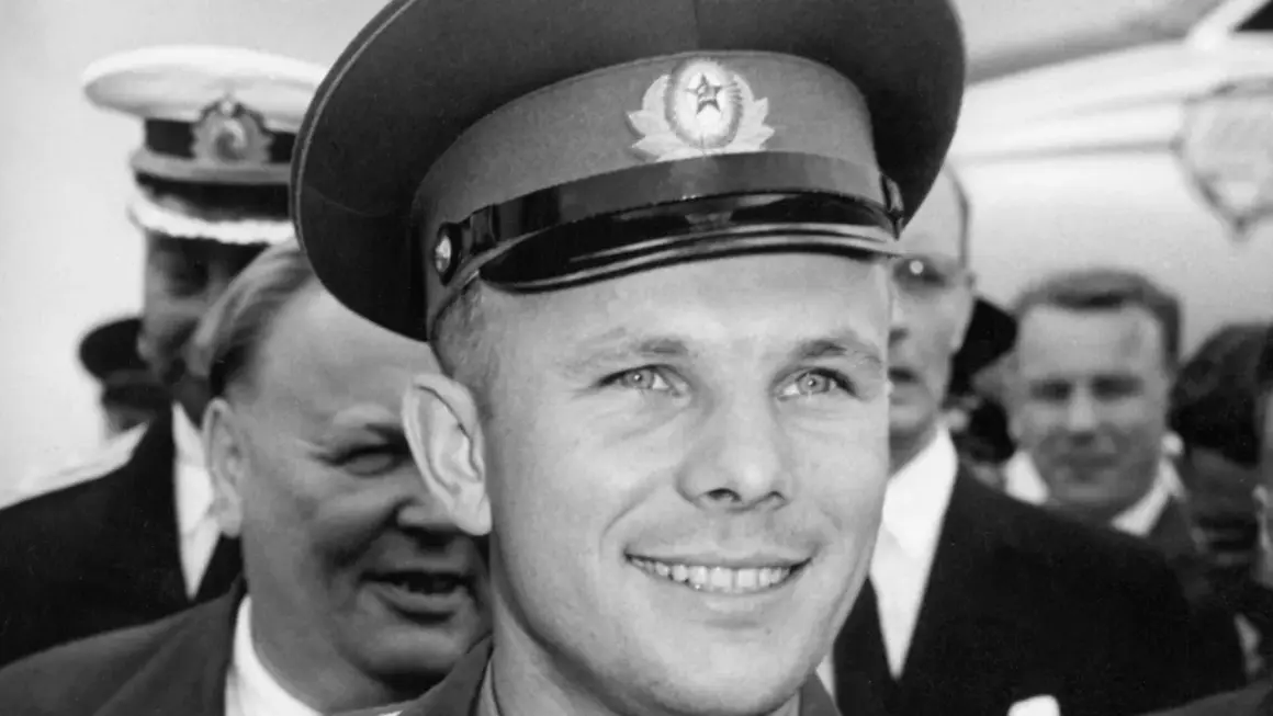 Juri Gagarin, den första människan i rymden, ler mot kameran. Han bär en rymdkeps med en sovjetisk symbol.