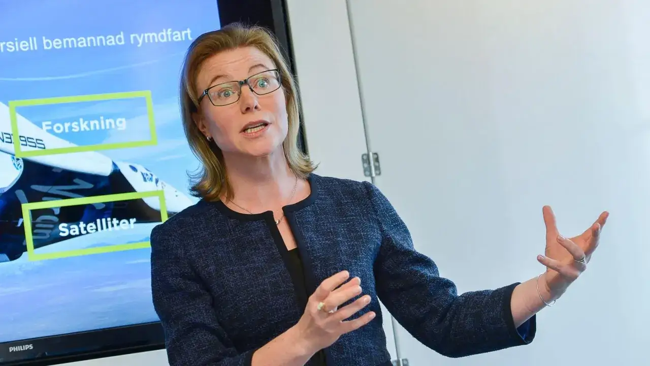 Karin Nilsdotter, med glasögon, gestikulerar framför en skärm som visar