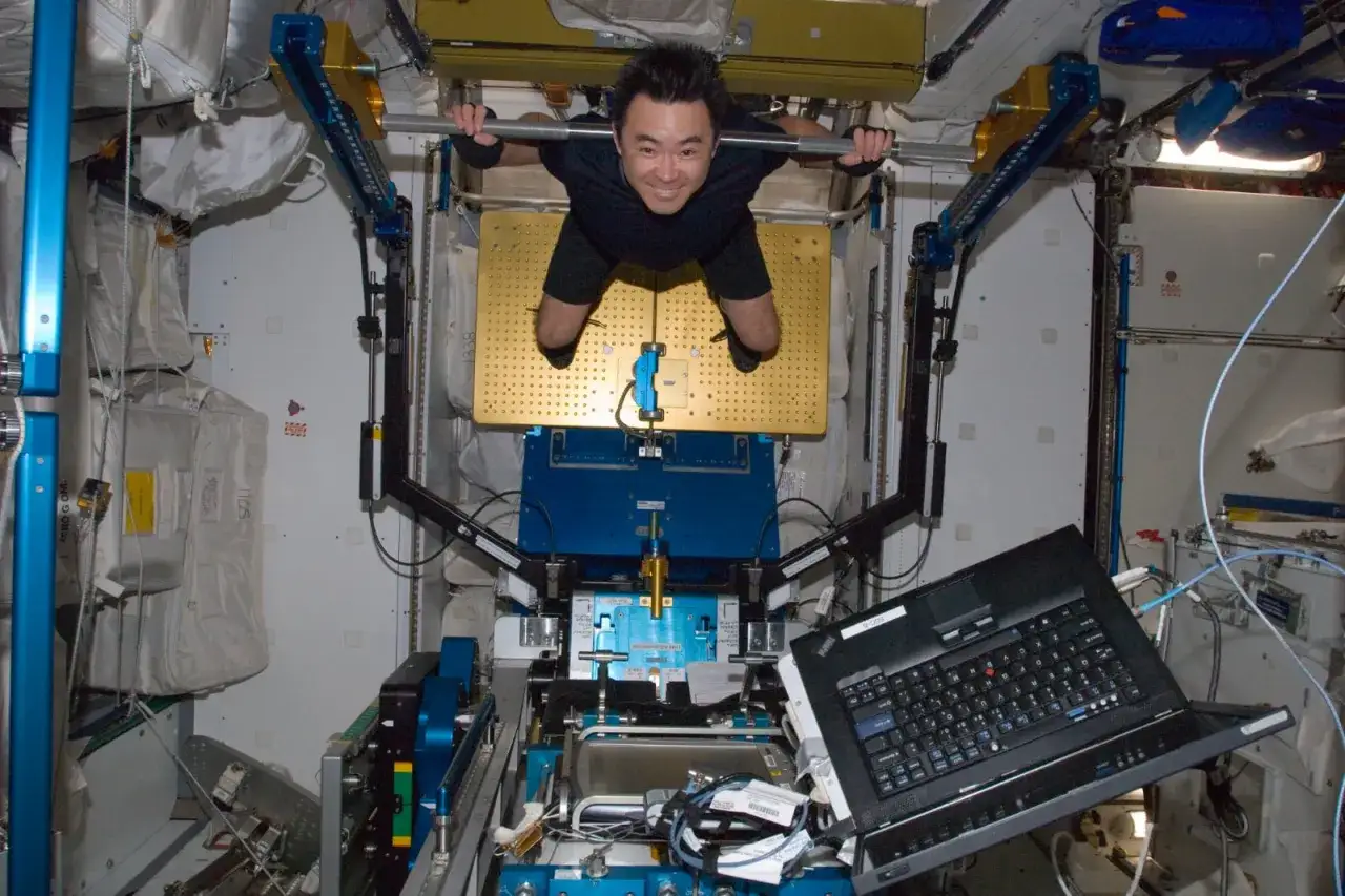 En astronaut tr&auml;nar i rymden, h&auml;ngande i en st&aring;ng. Han ler mot kameran, omgiven av utrustning och kablar.
