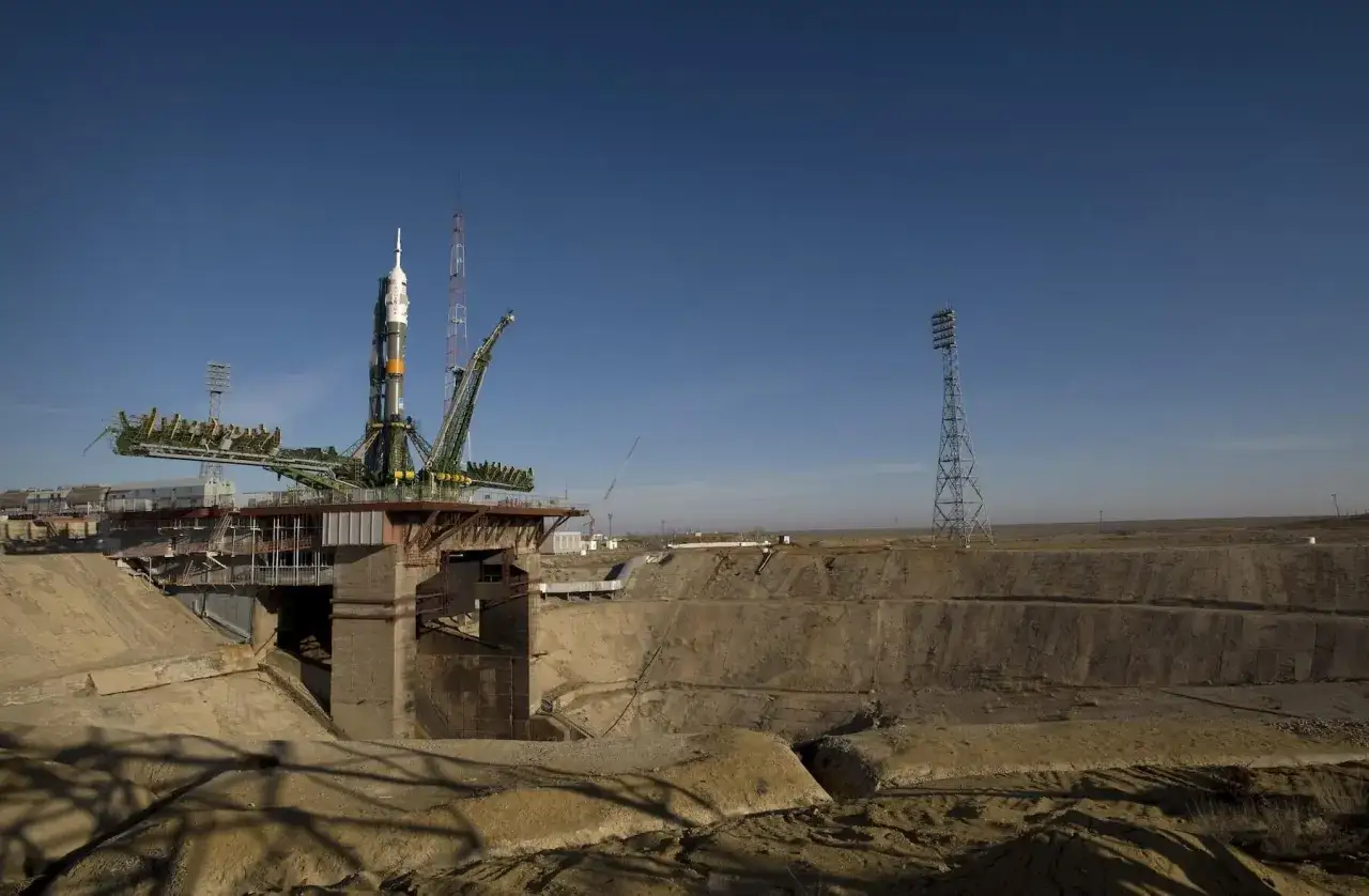 Raket redo f&ouml;r uppskjutning vid Baikonur kosmodrom. En stor raket st&aring;r p&aring; en uppskjutningsplattform, omgiven av en &ouml;de landskap och h&ouml;ga torn.