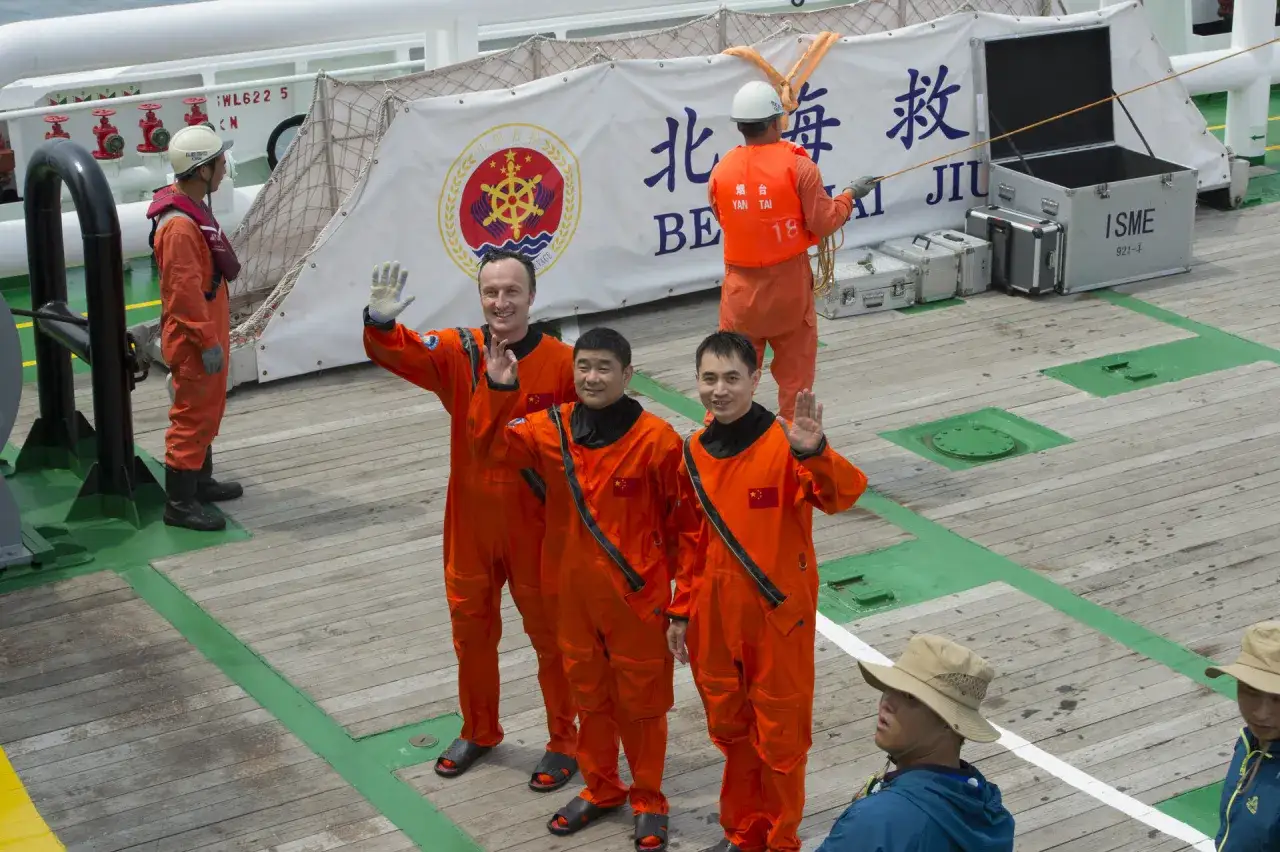 Tre m&auml;n i orange dr&auml;kter, som p&aring;minner om astronauter, vinkar glatt p&aring; ett fartyg. Kanske &auml;r de redo f&ouml;r ett rymd&auml;ventyr!