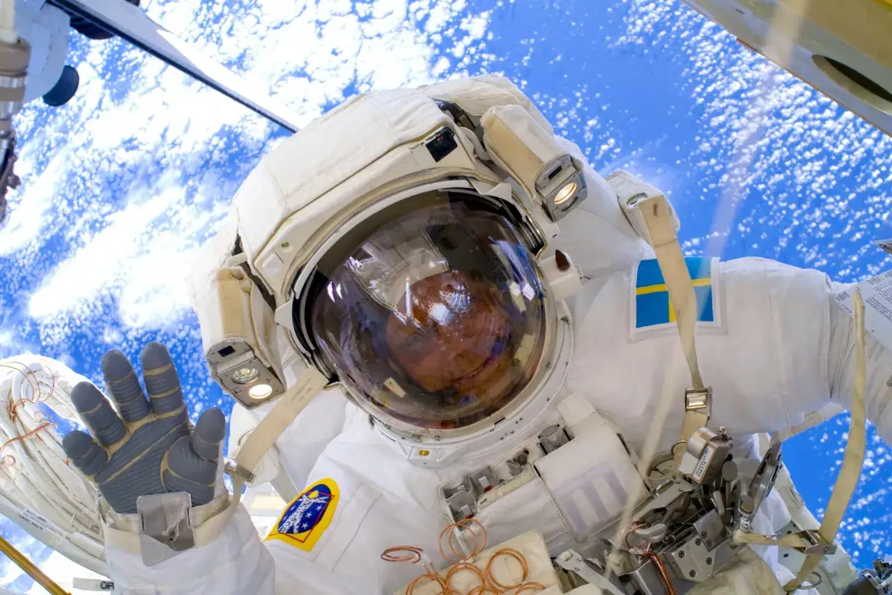 Astronaut Christer Fuglesang vinkar från rymden, med jorden synlig under.