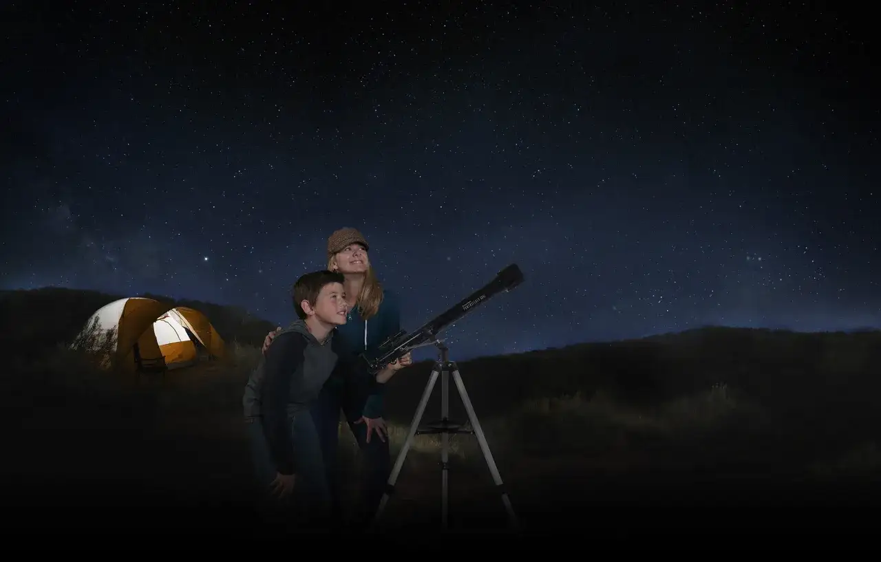 Mamma och son tittar på stjärnorna med teleskop. Kanske en framtida astrofysiker upptäcker universum. Tält i bakgrunden.