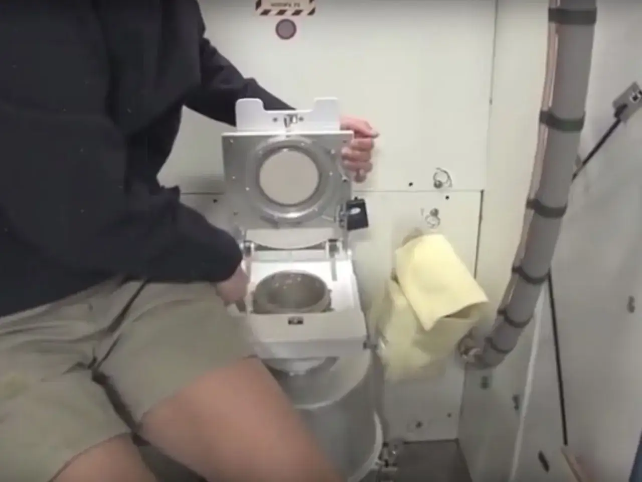 En astronaut demonstrerar hur bajsar man i rymden med en speciell toalett.